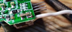 Circuit Board with Soldered Pins and Wire Close-up of a circuit board with vertically attached pins and a white wire soldered to one of the connections.