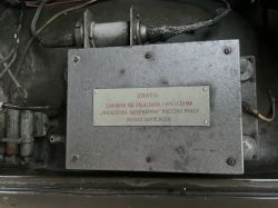 Szara metalowa skrzynka z tabliczką „UWAGA!” i przewodami w komorze pojazdu