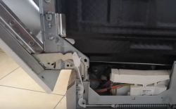 Wnętrze drzwi zmywarki z widocznym mechanizmem zawleczki i kablami.