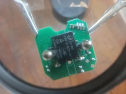 Close-up of an electronic module with a JIEYING integrated circuit mounted on a green PCB, held by a metal tool.