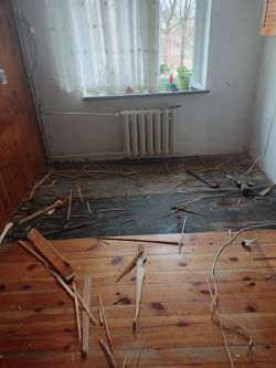 Rozebrana podłoga w kuchni z cienkimi, wysuszonymi deskami.