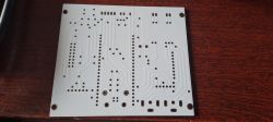 White printed circuit board with multiple holes and traces on a dark wooden background.