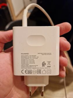 Ładowarka Huawei trzymana w ręku, pokazująca specyfikacje techniczne na etykiecie.