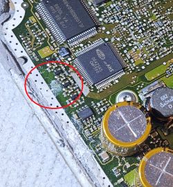 Zbliżenie na płytkę drukowaną z elektroniką, z zaznaczonym na czerwono miejscem uszkodzenia i śladami lutowania.