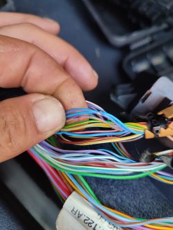 Zbliżenie na rękę trzymającą wiązkę kolorowych przewodów w samochodzie.