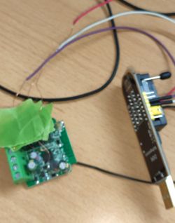 Blurry image of a circuit board with wires connected to a programmer attached to a USB port.