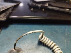 Zniszczony kabel spiralny z pękającą izolacją na ciemnym tle.