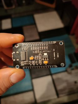 Bottom side of a PCB with SMD parts held between fingers; printed text “V660” and “NodeMcu v3”.