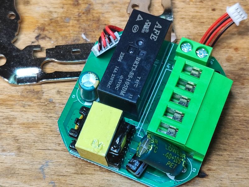 Close-up of a circuit board with a relay and green screw terminal block on a wooden surface