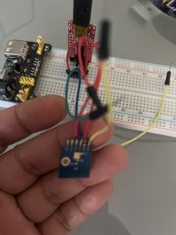 Person holding a small blue module connected to a breadboard with colored wires.