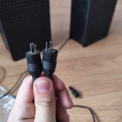 Dwa głośniki z kablami zakończonymi niestandardowymi wtyczkami trzymanymi w ręku.