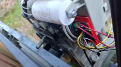 Zbliżenie na podłączenia elektryczne sterownika napędu bramy z widocznymi przewodami i kondensatorem.