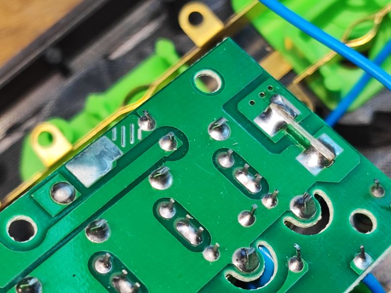 Zbliżenie na płytkę drukowaną z widocznymi, słabej jakości lutami i wystającymi nóżkami elementów elektronicznych.