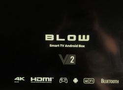 Zbliżenie na logo BLOW Smart TV Android Box V2 na czarnym tle, z ikonami 4K, HDMI, WiFi, Bluetooth i Android.