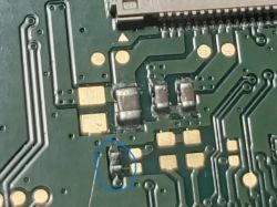 Zbliżenie na płytkę drukowaną z nieoznaczonym elementem elektronicznym zaznaczonym niebieskim kółkiem.