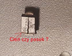 Zbliżenie elementu elektronicznego na szarej powierzchni z czerwonym napisem „Cień czy pasek ?”