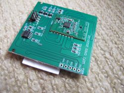 Close-up of a green PCB with electronic components and pin headers, lying on a light carpet.