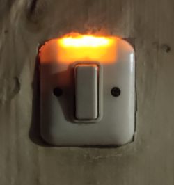 Świecąca pomarańczowo lampka przy włączniku światła na ścianie