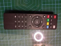 Black “TV Control” remote with OK button, number pad, and colored keys on a green grid cutting mat