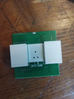 Green PCB module with white plastic buttons labeled WIFI-W6B on a wooden surface.