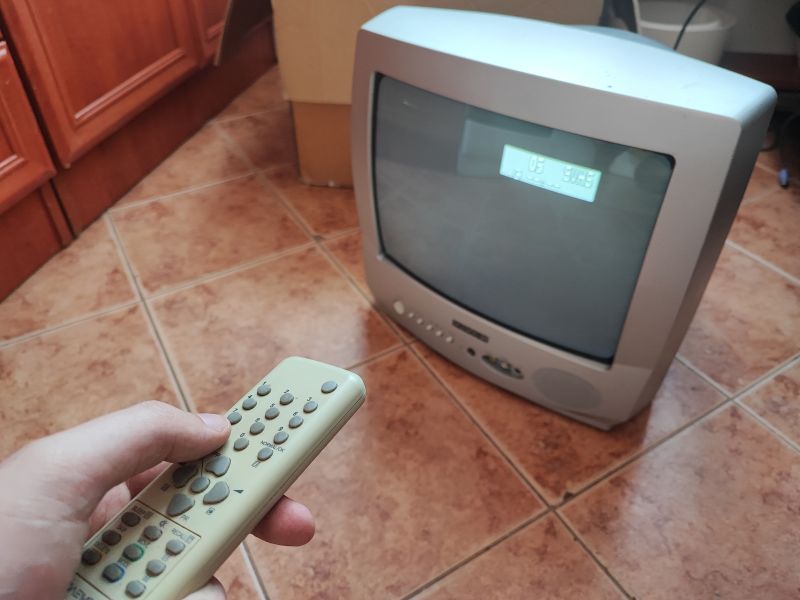Telewizor kineskopowy Daewoo K14C5GT z pilotem w ręku, ekran włączony, w tle widok kuchni.