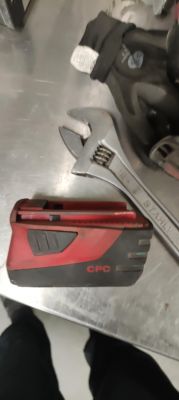 Czerwono-czarny akumulator Hilti CPC na metalowym stole, obok klucza francuskiego.