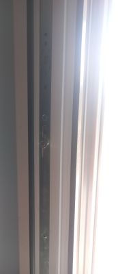Zbliżenie na mechanizm ryglujący okna z metalowymi elementami na ramie.