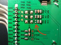 Close-up of a green PCB with SMD parts and a red curved arrow pointing to a component area