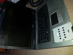Stary laptop Acer z wyjętym dyskiem twardym na tle dywanu.