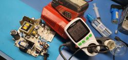 Disassembled battery charger on a workbench with an energy meter displaying voltage.