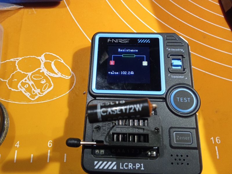 Tester LCR-P1 mierzący rezystor 102,2 Ω na tle żółtej maty roboczej