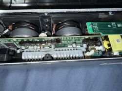 Wnętrze urządzenia elektronicznego z widoczną płytą główną, głośnikami i uszkodzonym kondensatorem