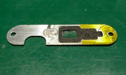 Metalowy element z wycięciem i otworami, z czarną wkładką, na zielonej macie