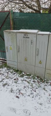 Skrzynka elektryczna ZK 6699 przy ogrodzeniu, pokryta śniegiem.