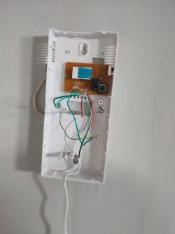 Otwarta obudowa domofonu z widocznymi kablami i płytką drukowaną na ścianie.