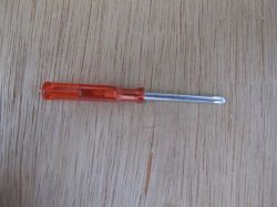 Small Screwdriver on Wooden Background Small screwdriver with a transparent orange handle lying on a wooden surface.