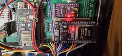 Close-up of PCBs with an ESP32 module, a smaller board, and multicolored wiring; indicator LEDs are lit.