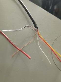 Zdjęcie zestawu luźnych kabli z instalacji kamery cofania, obejmujących przewody w kolorach: czerwonym, białym, żółtym i jednym bez izolacji.