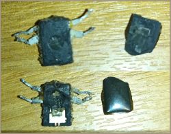 Uszkodzony element elektroniczny z pralki na tle drewnianym.