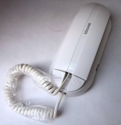 Biały unifon BTicino z przewodem spiralnym, leżący na jasnej powierzchni.