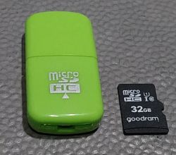 Zielony czytnik kart microSD oraz karta microSD 32 GB marki Goodram na szarej powierzchni.