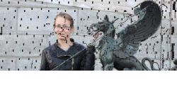 Osoba stojąca obok metalowej rzeźby gryfa; obraz z zakłóceniami graficznymi.