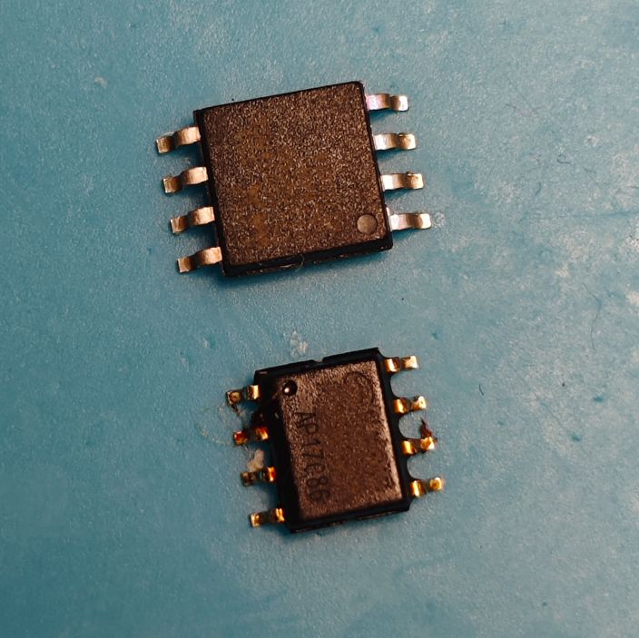 Two black SOIC-8 IC chips on a blue surface, a larger one on top and a smaller one below.