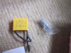 A yellow CHAMPION X2 MPX 3.3µF capacitor with two black wires and two metal screws in a plastic bag on a beige carpet.
