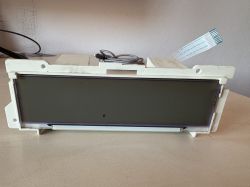 Stary wyświetlacz elektroniczny leży na stole, z widocznym złączem taśmowym.