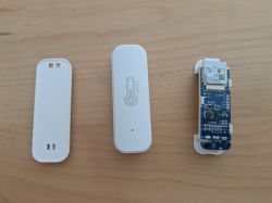 Three parts of a disassembled WiFi thermometer: back cover, front case with thermometer symbol, and electronic circuit board.