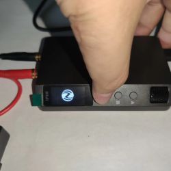 Close-up of DP100 power supply with active screen and a hand pressing a front button