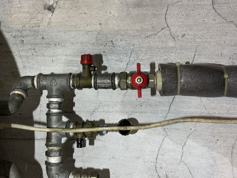 Rury instalacji wodnej z czerwonym odpowietrznikiem i czerwonym zaworem na tle betonowej ściany