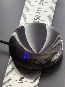 Round Electronic Device on a Ruler A black, round electronic gadget connected by cable lies on a ruler with a millimeter scale.
