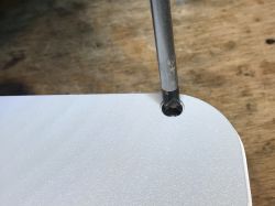 A spanner screwdriver unscrewing a screw from a white enclosure on a wooden surface.